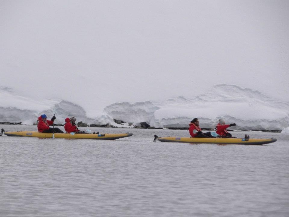 Two yellow kayaks with a pair of man and woman each with red jackets while kayaking in Antarctica 
