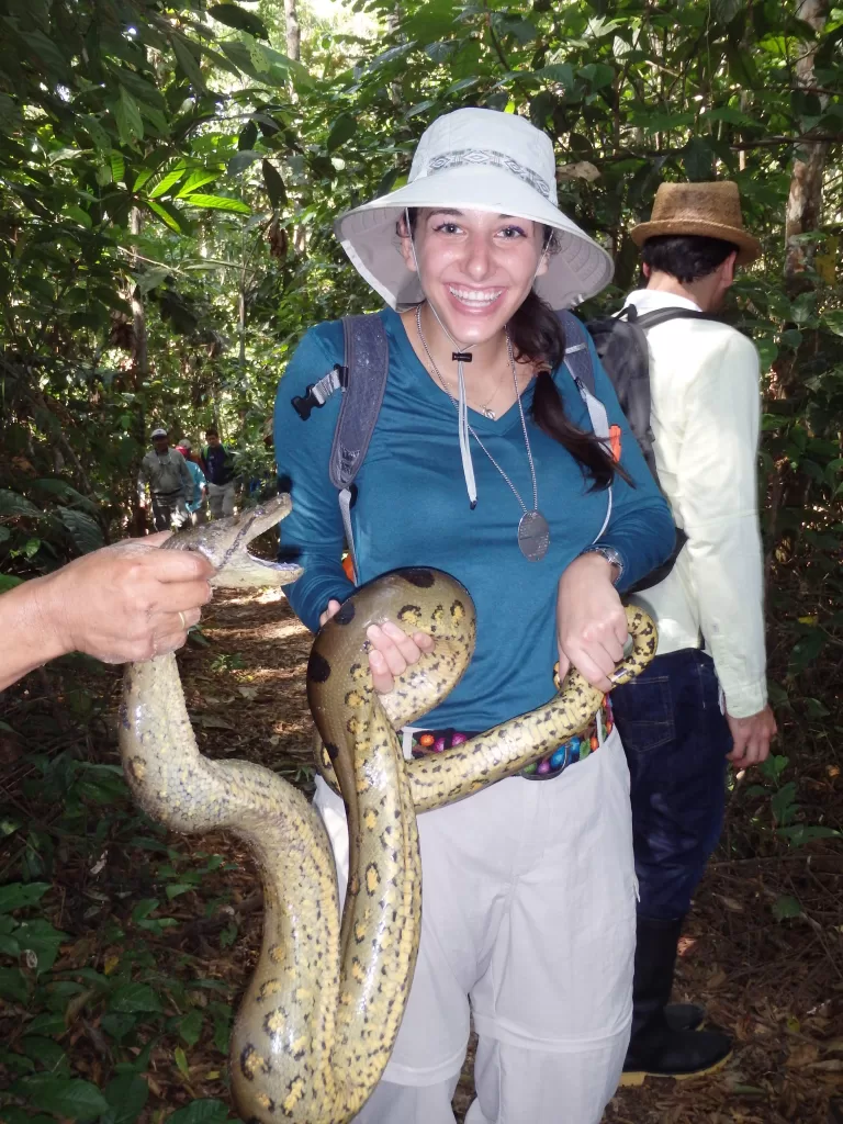 Woman with a hat and blue shirt holding an anaconda snake in the Amazon in Peru