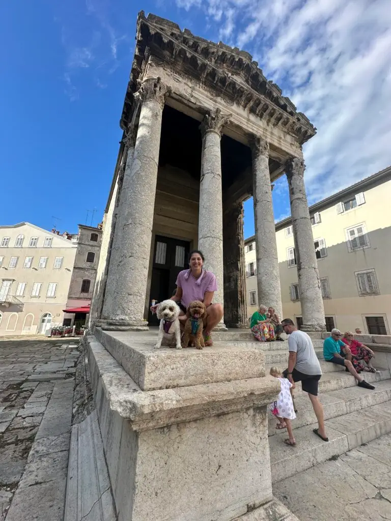 Woman in pink shirt with two cockapoo dogs in front of of the Temple of Augustus in Pula Croatia