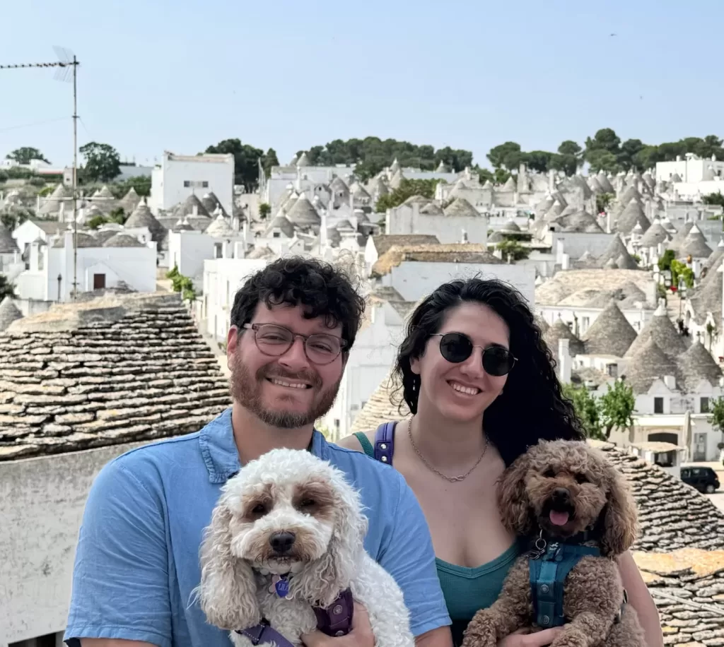 My husband, two dogs and I with the trulli houses of Alberobello in Puglia in the background