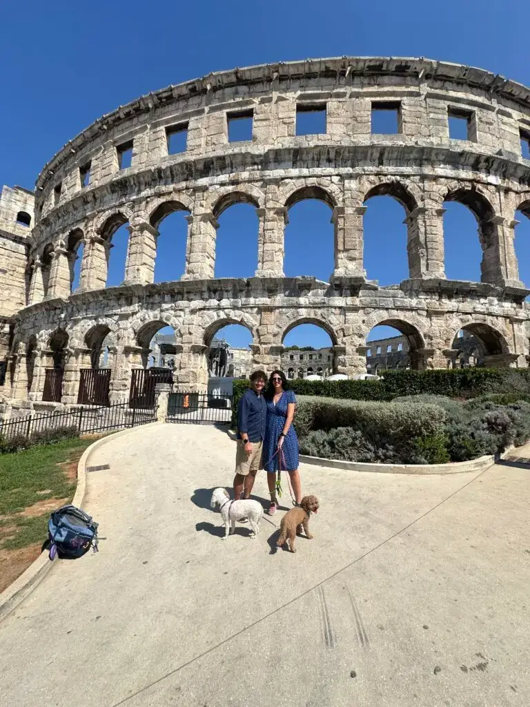 Two people and two dogs in front of the Pula Arena or Pula Amphitheatre which is one of the main things to do in Pula with dogs
