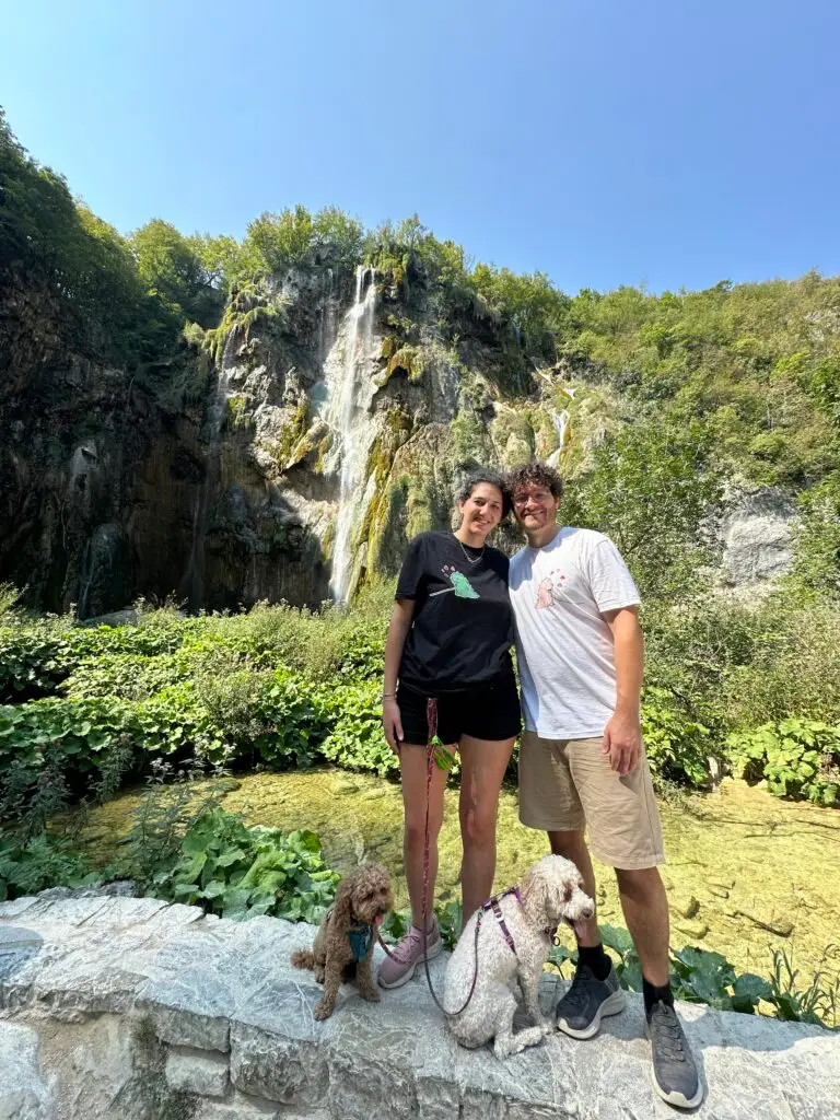 One of Plitvice’s waterfalls in the background and in front a woman, a man and two dogs  