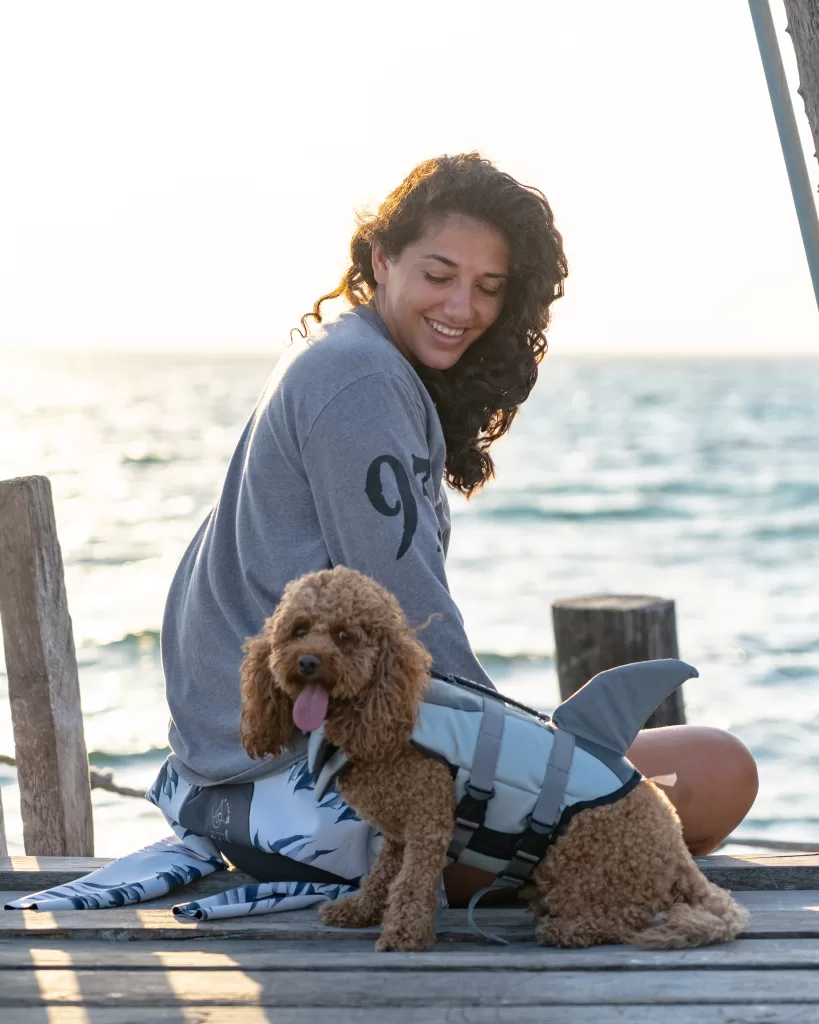 Me and my dog Mishka on a dock overlooking the Caribbean in Xcalak Mexico, I am wearing a grey long sleeve shirt while Mishka is wearing a shark fin dog life vest