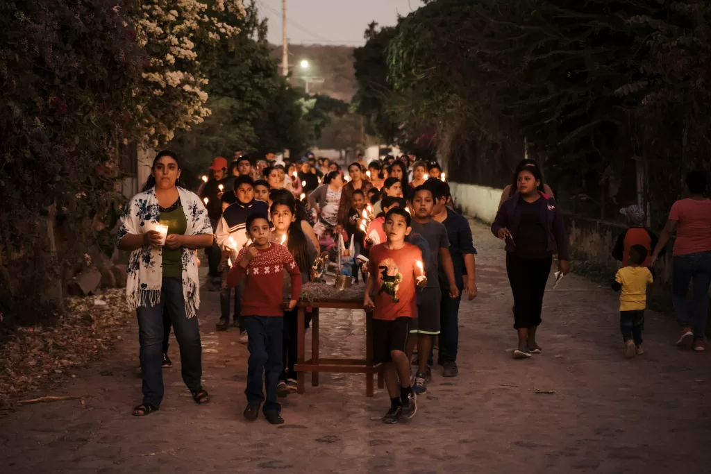 Group of people during a posada carrying a nativity scene and candles while singing asking for lodging