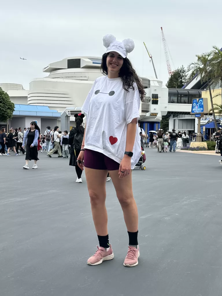 Woman standing in Disneyland Tokyo with a Baymax white tshirt, red shorts and white cap with mickey pompom ears
